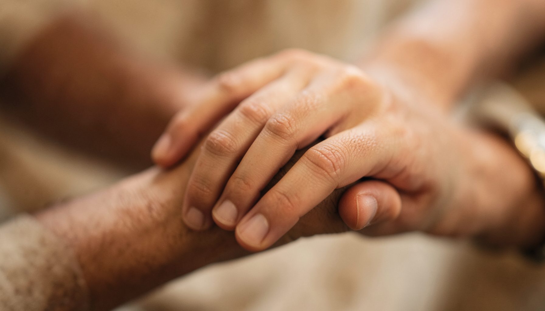Gros plan flou d'une main posée sur une autre main, tons chauds de brun et beige, ambiance douce et solidaire