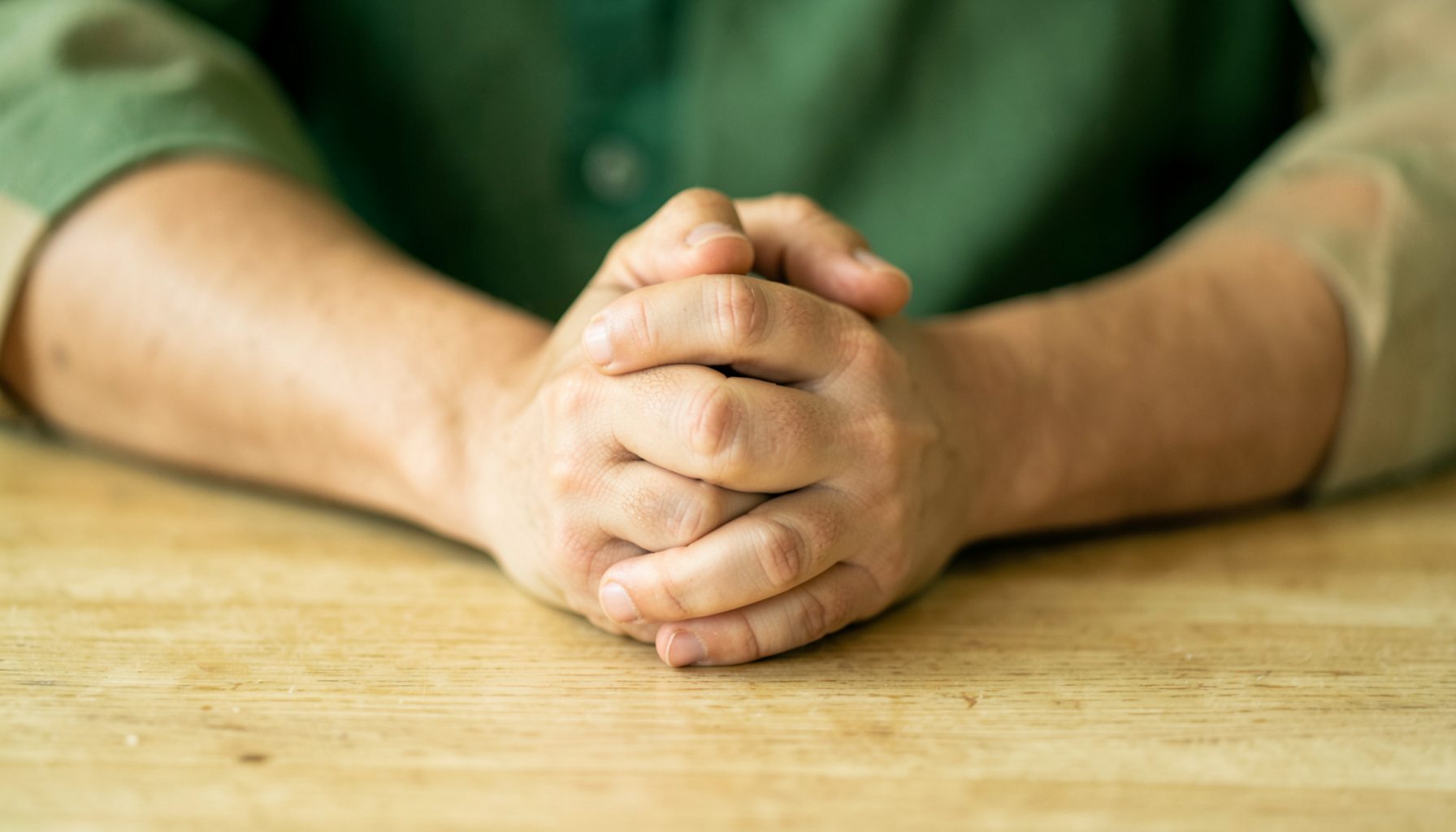 Deux mains jointes sur une table en bois, gestes de soutien dans des tons chauds de vert et beige